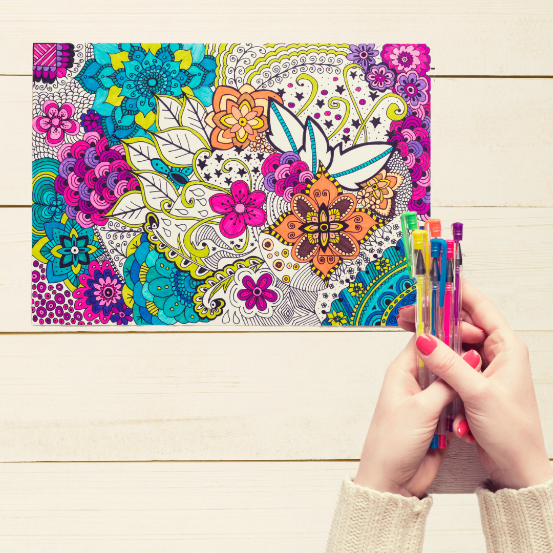 hands holding gel pens on a wood background and an adult coloring sheet