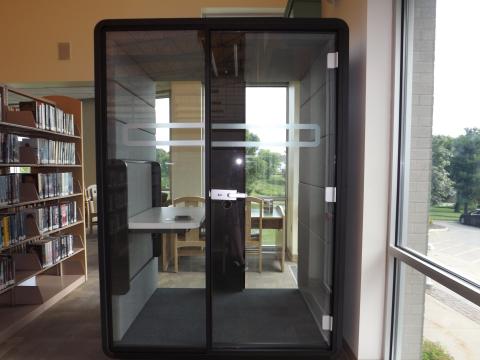 Personal study pod with two clear walls and two solid walls, with doors and desk.