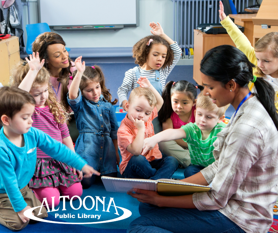 group of children on the floor watching a woman read a picture book